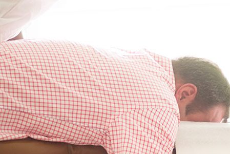 Ein Mann mit einem karierten Hemd liegt Bäuchlings auf einer Liege und bekommt eine Behandlung am Rücken.