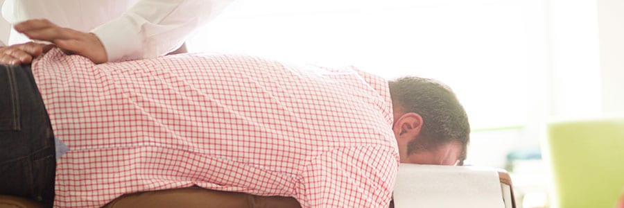 Ein Mann mit einem karierten Hemd liegt Bäuchlings auf einer Liege und bekommt eine Behandlung am Rücken.