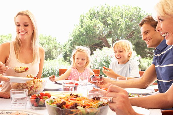 Eine lachende, fröhliche Familie, mit Mutter, Vater, Kinder und Großeltern sitzen am Tisch und essen zusammen.