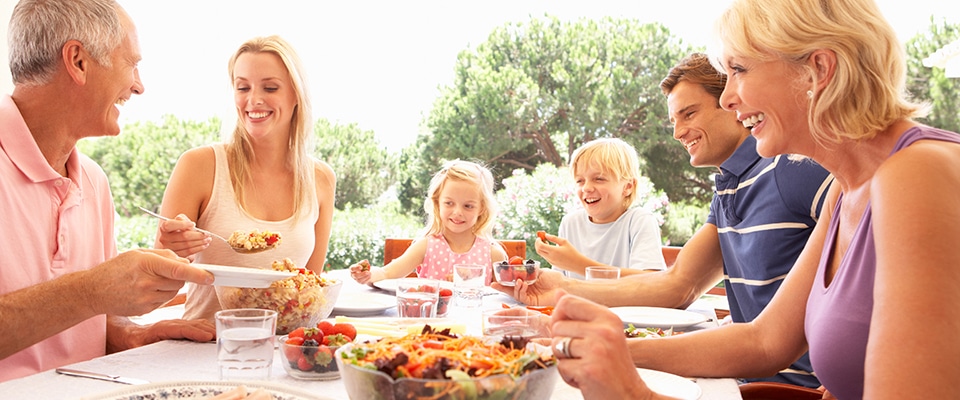 Eine lachende, fröhliche Familie, mit Mutter, Vater, Kinder und Großeltern sitzen am Tisch und essen zusammen.
