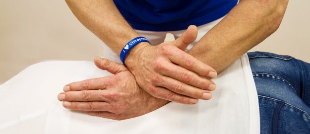 Justierung_Wirbelsäule Eine Person liegt Bäuchlings auf einer Liege und bekommt eine Behandlung am Rücken.