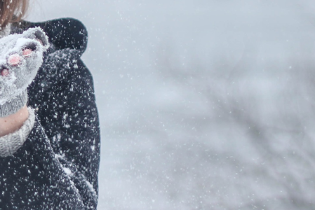 Eine Frau pustet Schnee von ihren Händen, die mit Fingerhandschuhe bedeckt sind.