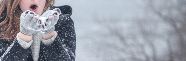 Den Winter genießen Eine Frau pustet Schnee von ihren Händen, die mit Fingerhandschuhe bedeckt sind.