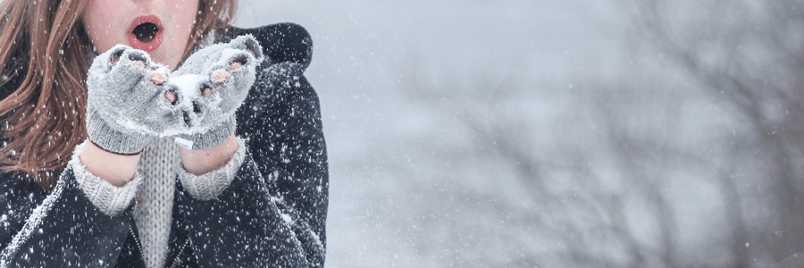 Den Winter genießen Eine Frau pustet Schnee von ihren Händen, die mit Fingerhandschuhe bedeckt sind.