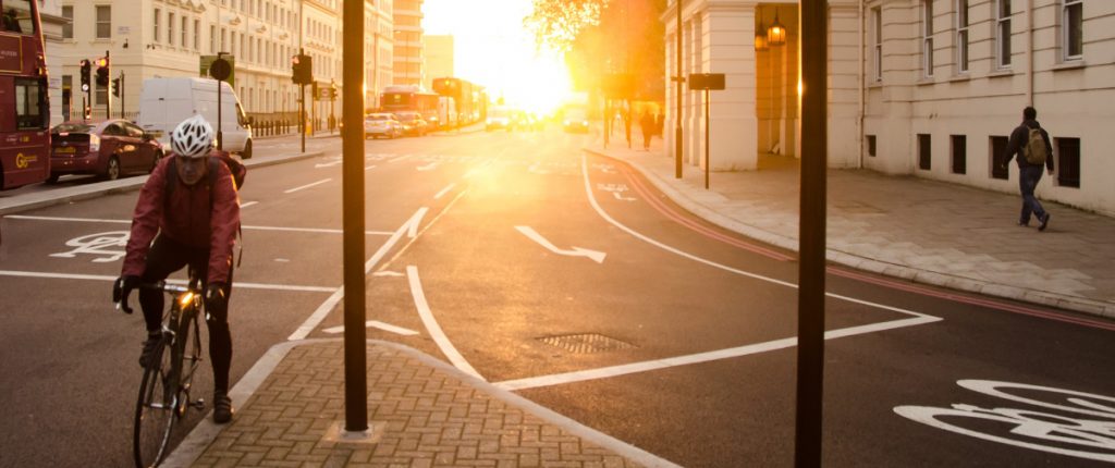 Ein Stadtbild mit einem Fahrradfahrer, vor einem Sonnenuntergang.
