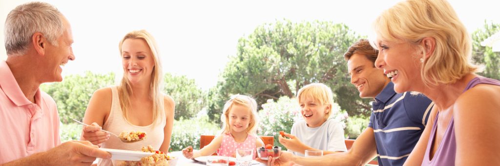 Eine lachende, fröhliche Familie, mit Mutter, Vater, Kinder und Großeltern sitzen am Tisch und essen zusammen.