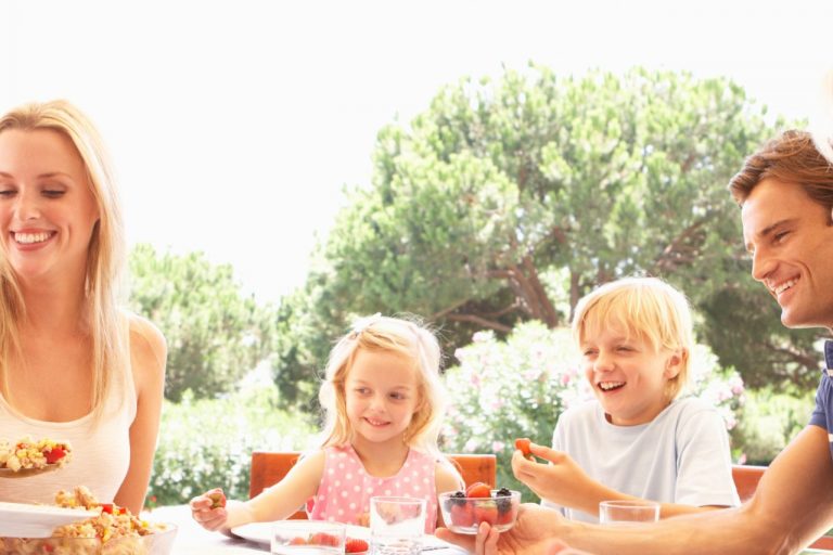 Eine lachende, fröhliche Familie, mit Mutter, Vater, Kinder und Großeltern sitzen am Tisch und essen zusammen.