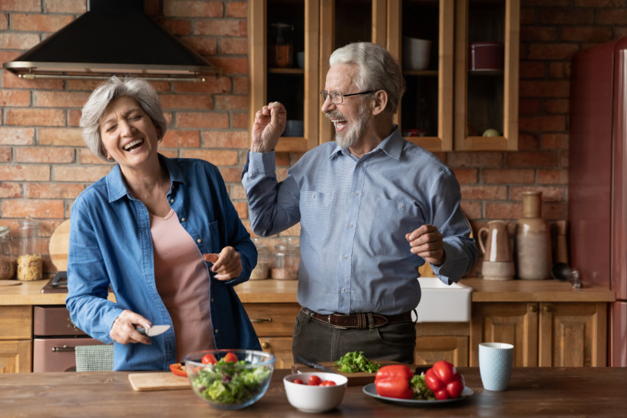 Überglückliches verheiratetes Familienpaar haben zusammen Spaß in der Küche bei der Zubereitung von Speisen, mit spielerischer Stimmung. Aufrichtiger glücklicher alter Mann und Frau lachen und kochen eine Mahlzeit zu Hause.