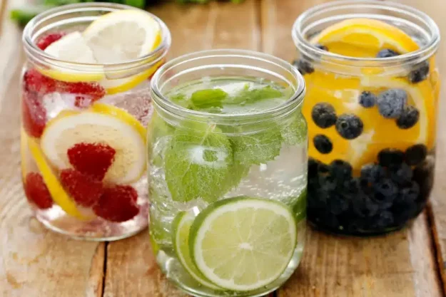 Fastenzeit_900x600 Drei Trinkgläser, die mit Wasser und verschiedenen Früchten gefüllt sind.