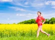 Eine junge Frau joggt durch ein Rapsfeld.