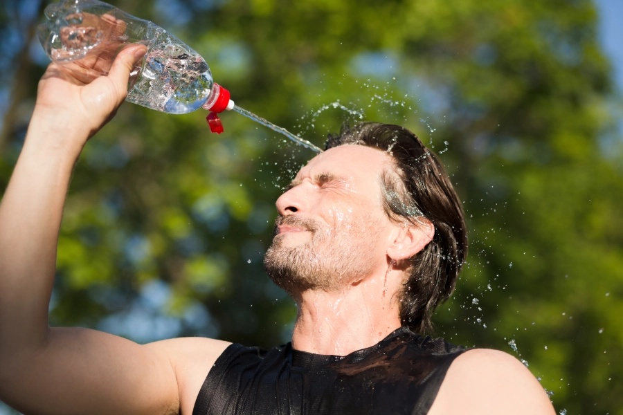 Ein Sportler, der sich Wasser aus seiner Trinkflasche ins Gesicht spritzt.